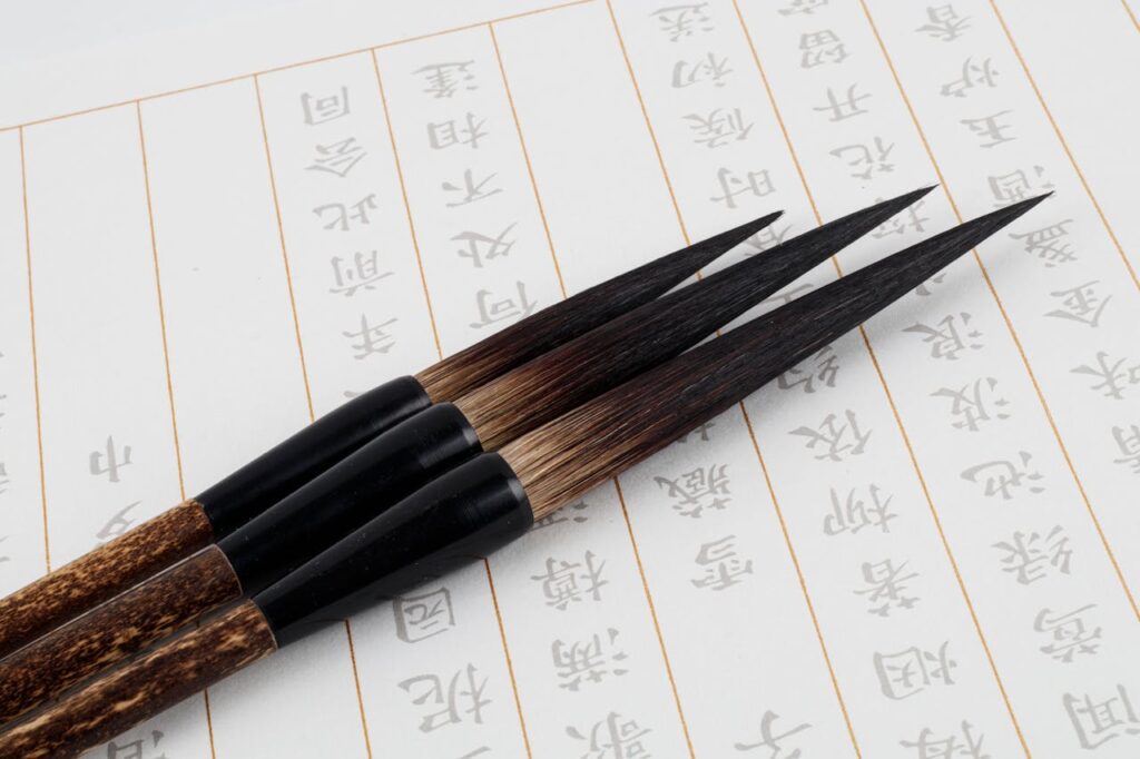 Three traditional calligraphy brushes positioned on Japanese script paper. Ideal for cultural and art themes.